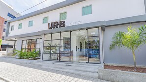 Un URB HOTEL con fachada moderna, grandes ventanales de vidrio y un pequeño árbol en la entrada.
