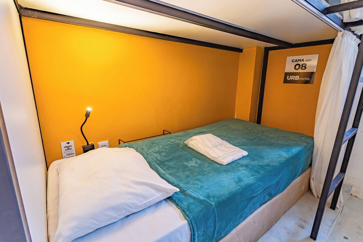 A single bed with a teal bedspread and white pillows in a room with yellow walls.
