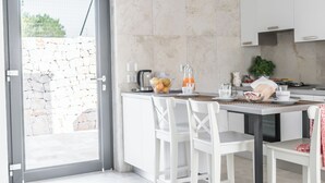 A modern kitchen with white cabinetry, a stone wall, and a dining area with white chairs.