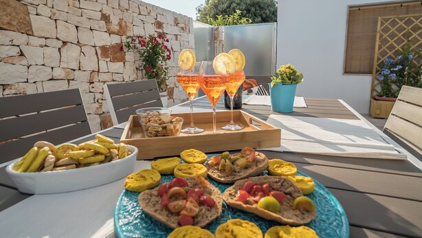 An outdoor dining area with a stone wall, wooden furniture, and a variety of food and drinks.