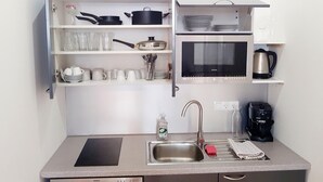 Eine kleine Küchenzeile mit Mikrowelle, Backofen und unterschiedlichem Küchenzubehör auf Regalen.