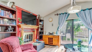 Een woonkamer met een rode bakstenen open haard, een televisie, een boekenkast en een eethoek met een tafel en stoelen.