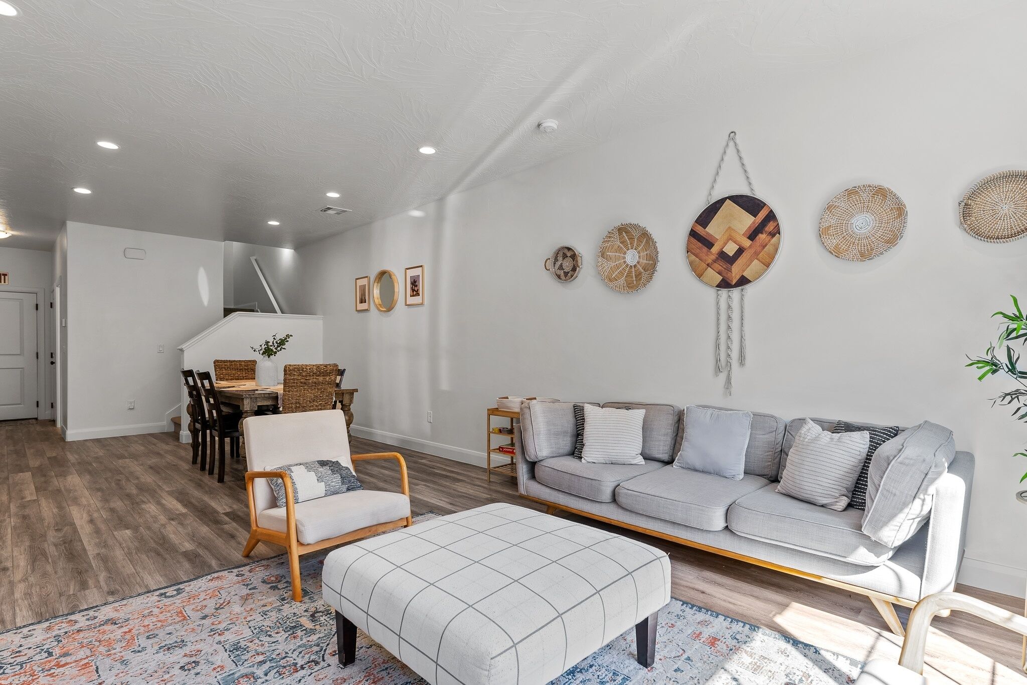 A modern living room with a grey sofa, a wooden coffee table, and a dining area with wicker furniture.