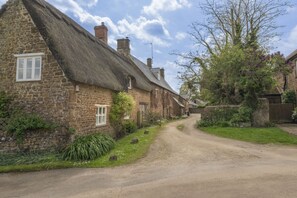 A narrow rural road flanked by traditional stone houses with thatched roofs. - Characterful dog friendly holiday cottage - The Granary at Oriel Farm (Shenington)