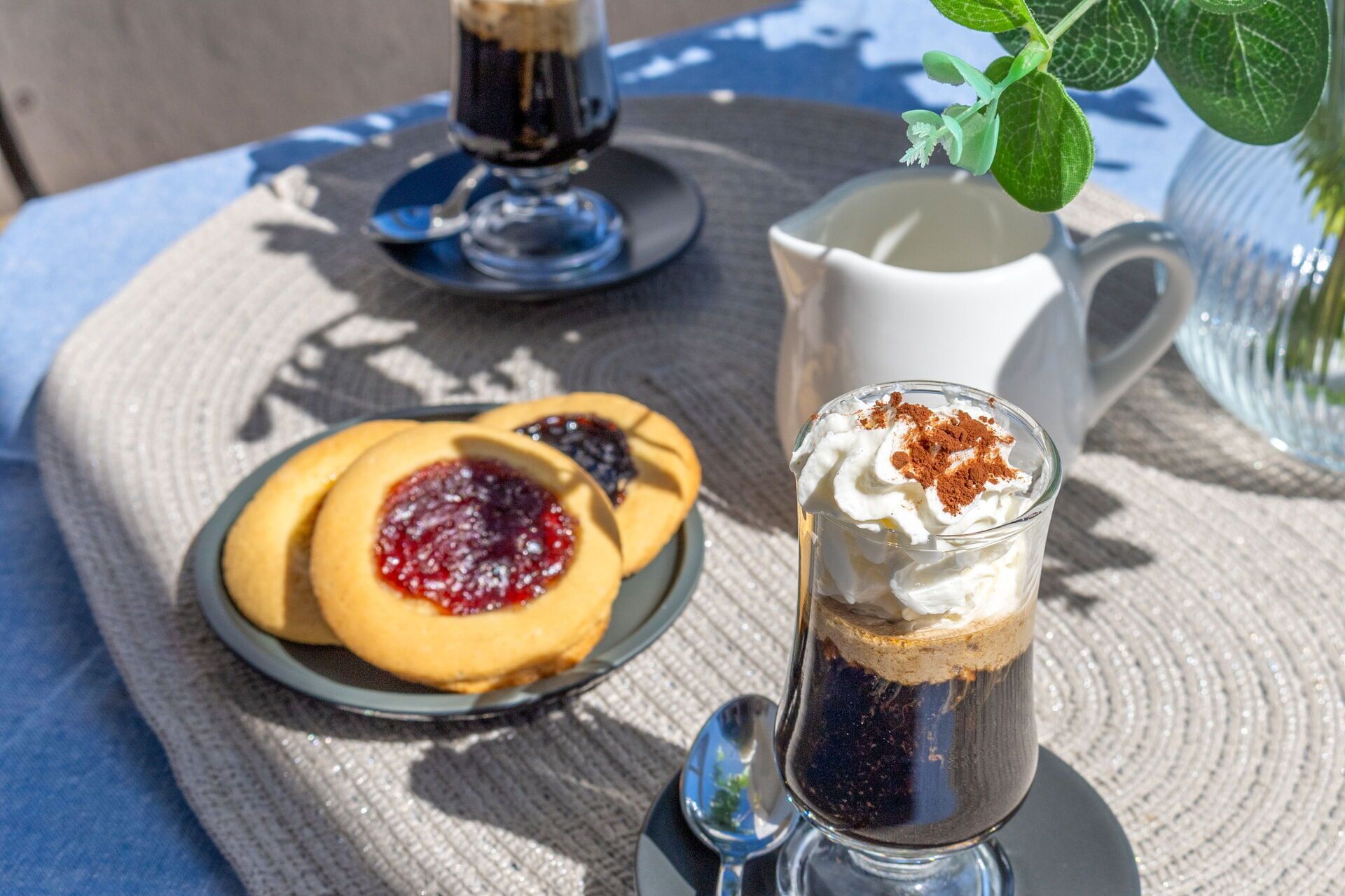 Eine Dessert-Anrichtung mit einer Kaffeetasse, einem Teller Kekse und einer Kanne auf einer gewebten Tischdecke.