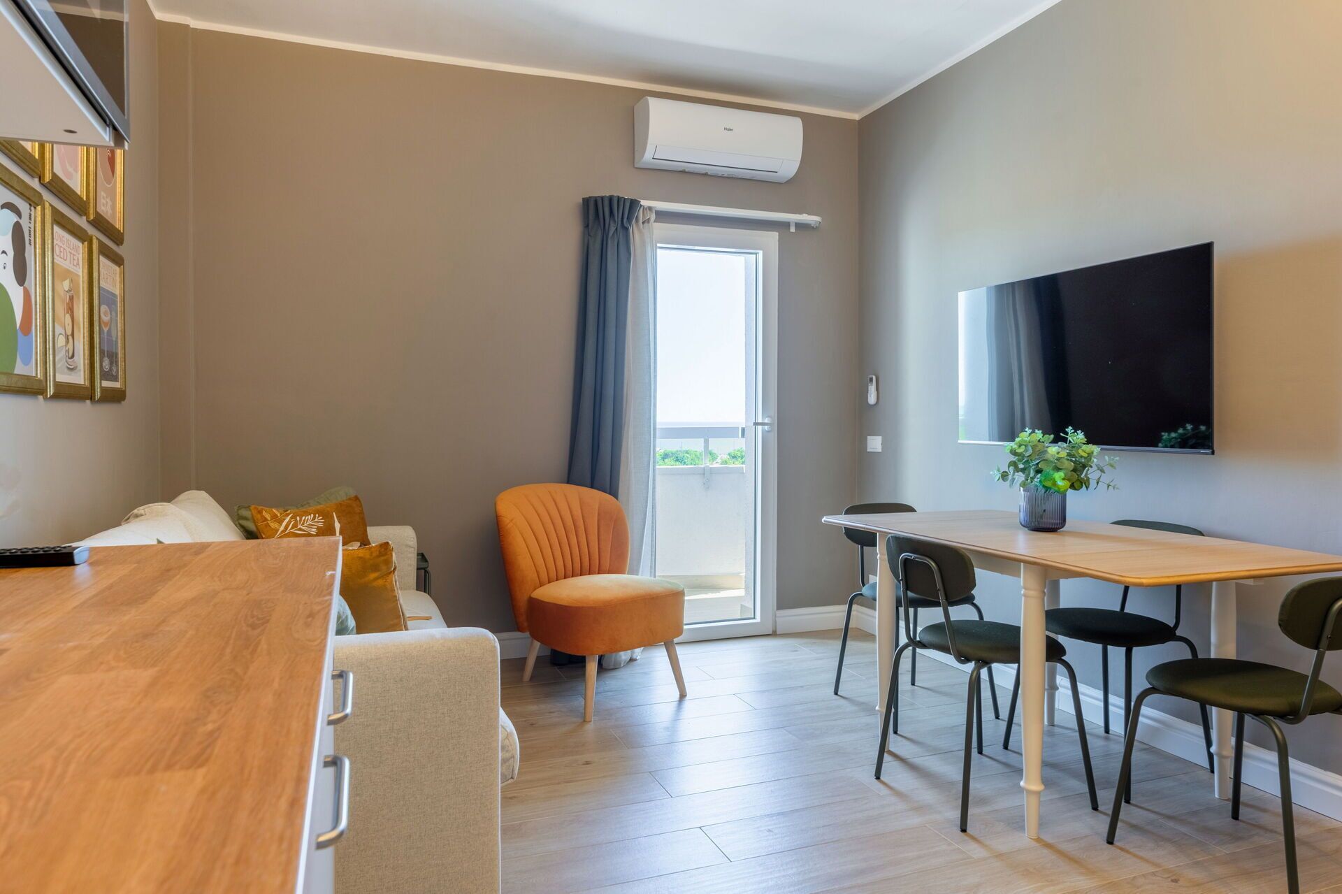 Un salon moderne comprenant un canapé, une table à manger avec des chaises, un téléviseur fixé au mur et une porte-fenêtre coulissante donnant sur un espace extérieur.