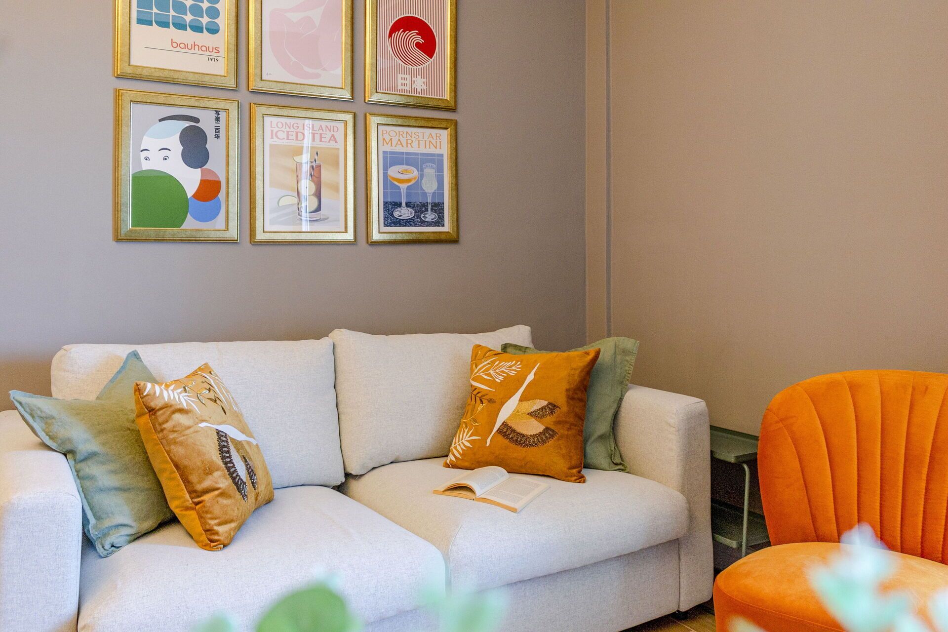A living room with a white sofa, orange armchair, and various framed artworks on the wall.
