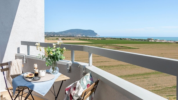 A balcony with a table set for two, overlooking a coastal landscape with fields and a distant mountain. - Italian Experience- Suite MareConero (Porto Recanati)