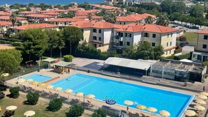 A large swimming pool with multiple lanes, surrounded by sun loungers and umbrellas, set against a backdrop of residential buildings and a clear sky. - Italian Experience- Suite MareConero (Porto Recanati)