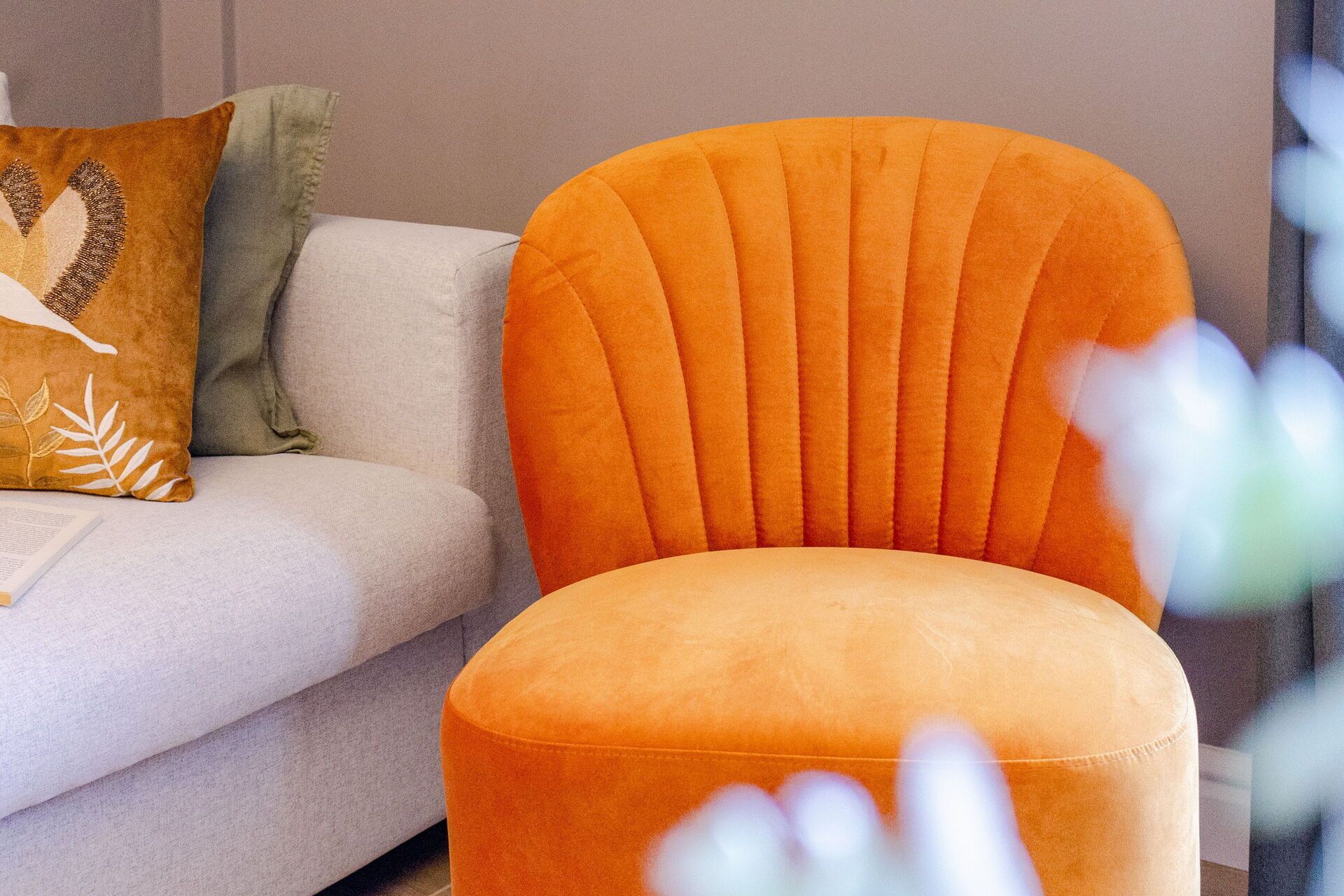 A modern living room with a light grey sofa and an orange armchair.