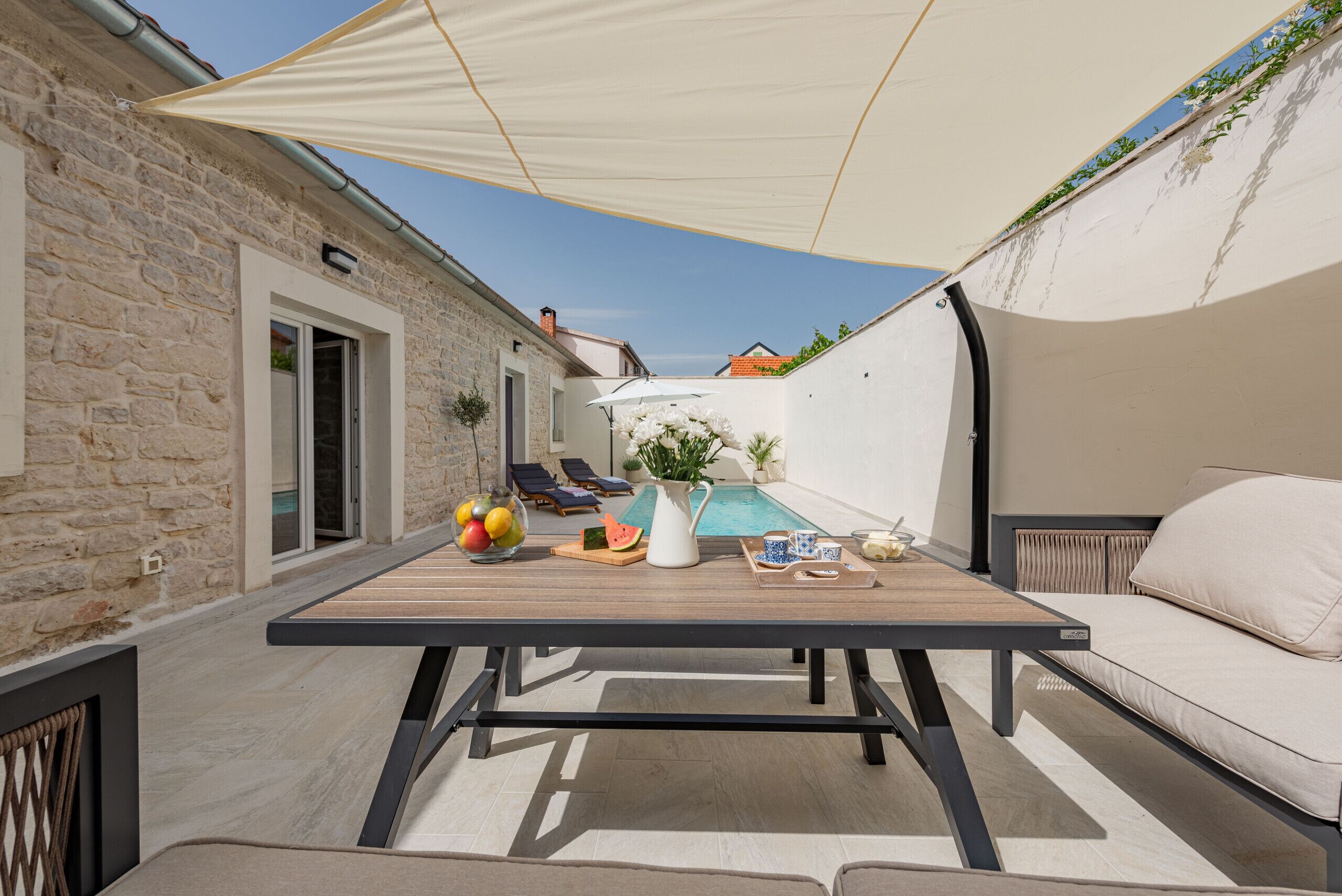 Eine Terrasse mit gedecktem Tisch, ein Pool im Hintergrund und ein Steinhaus.