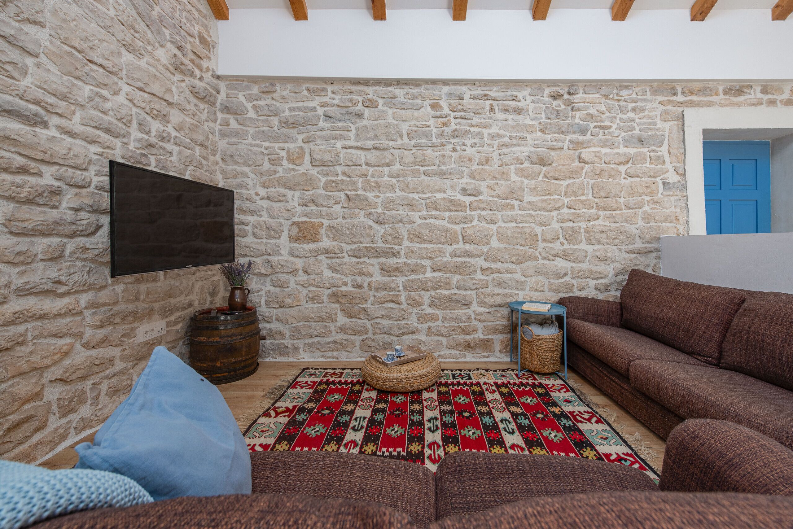 A cozy living room with a stone wall, a flat-screen TV, a patterned rug, and a brown sofa.