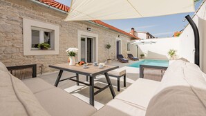A stone building with a tiled roof, a pool, outdoor seating, and a large umbrella. - Villa Pod Murvom (Novigrad)