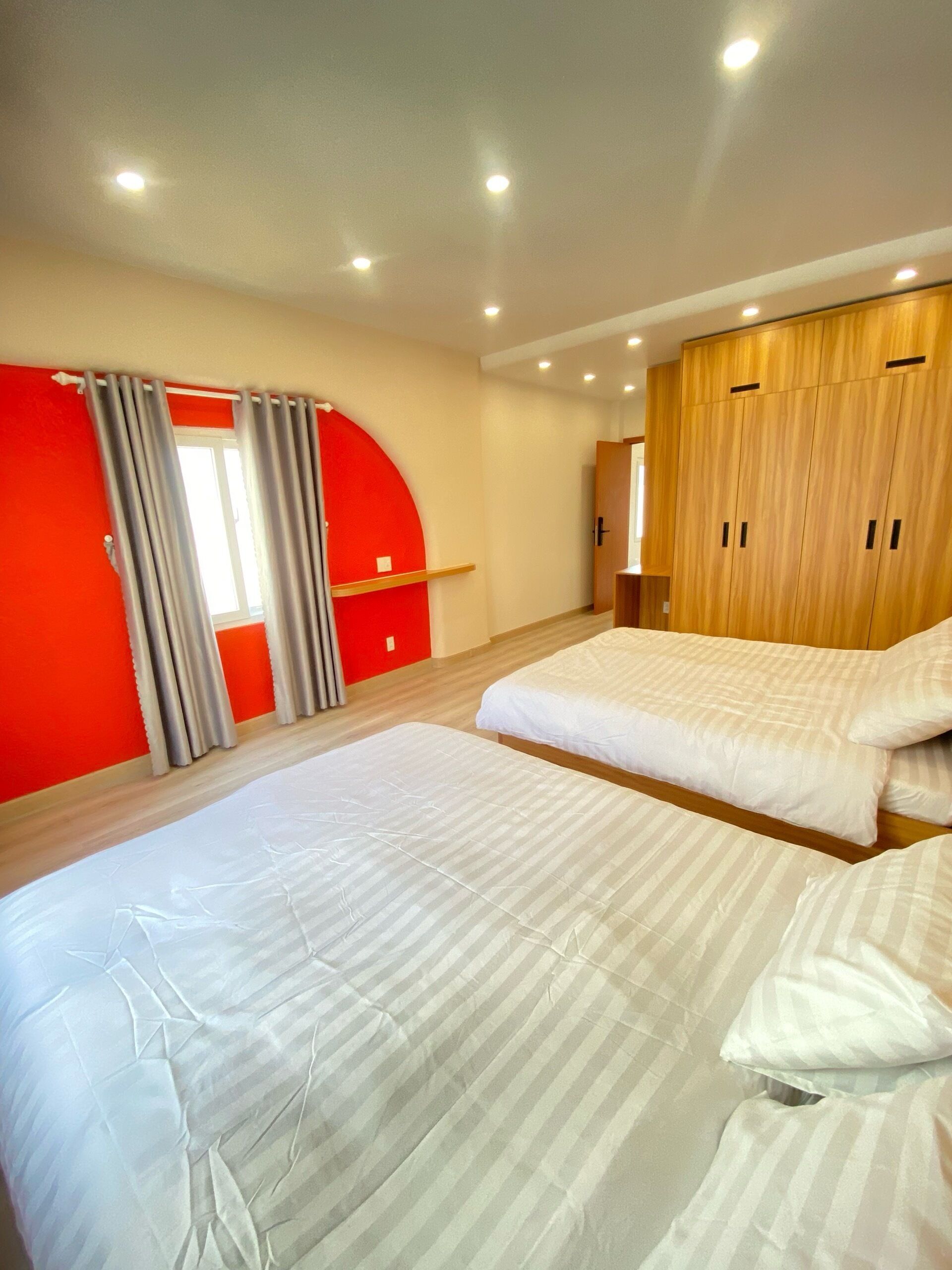 Un dormitorio con dos camas, un armario de madera y una pared de acento roja.