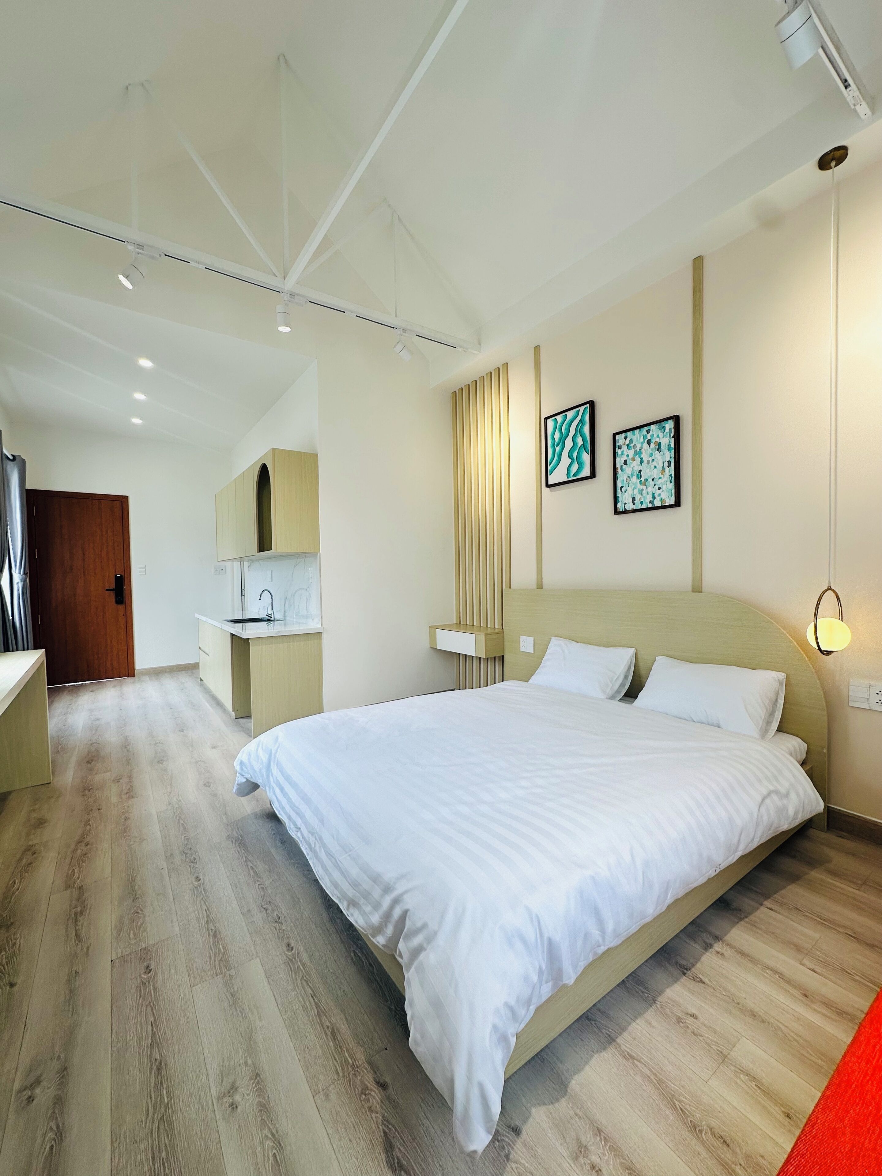 Ein modernes Hotelzimmer mit einem großen Bett, einem integrierten Schreibtisch, einer kleinen Küchenzeile und Kunstwerken an den Wänden.