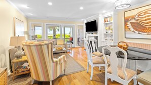 A spacious living room with a sofa, armchairs, a dining table, and a TV. - Beach Club Villa 38 - Oceanfront Gem! Walkout! (Isle of Palms)
