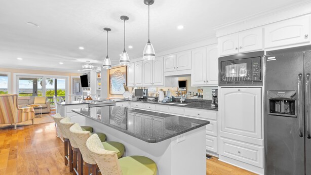 A modern kitchen with white cabinets, a large island with bar stools, stainless steel appliances, and pendant lighting. - Beach Club Villa 38 - Oceanfront Gem! Walkout! (Isle of Palms)