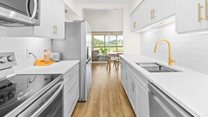 A modern kitchen with white cabinetry, stainless steel appliances, and a wooden floor. - Fairway Dunes 14 - Tennis! Pool! Beach! (Isle of Palms)