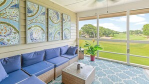A sunlit room with a blue sofa, a coffee table, and a large window offering a view of a golf course. - Fairway Dunes 14 - Tennis! Pool! Beach! (Isle of Palms)