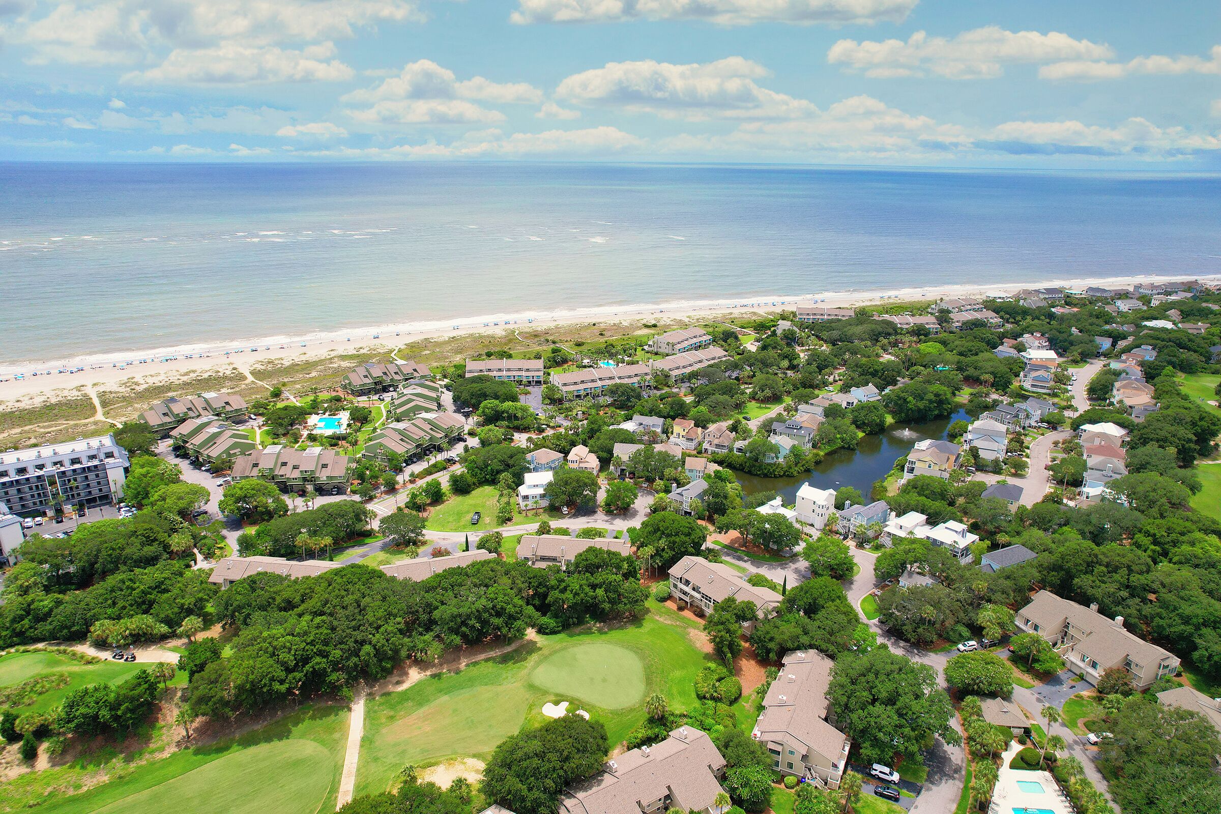 An aerial view of a coastal residential area with houses, a golf course, and a beach.
