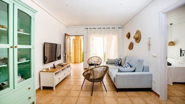 Een woonkamer met een bank, een televisie, een rieten fauteuil en een kast.
