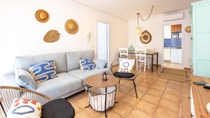Een woonkamer met een bank, stoelen, een ronde tafel en een keuken die door een open deur zichtbaar is.