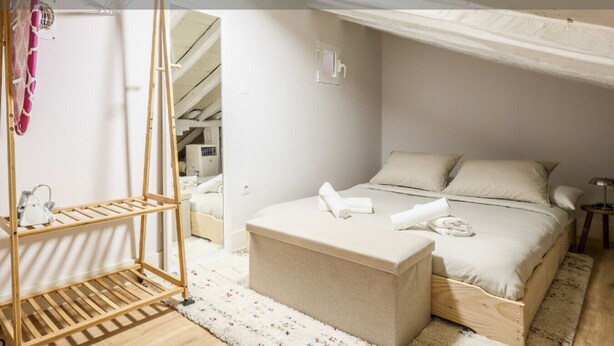 A bedroom with a bed, a wooden bench, a hanging rack, and a small table. - Charming Central Madrid Loft (Madrid)