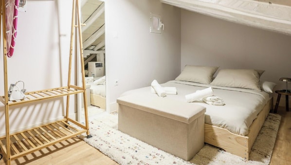 Un dormitorio con una cama, un banco de madera, un perchero y una mesita.