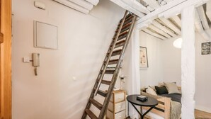 A room with a wooden ladder leaning against the wall, a small wooden bed, a bedside table, and a wall-mounted light fixture. - Charming Central Madrid Loft (Madrid)
