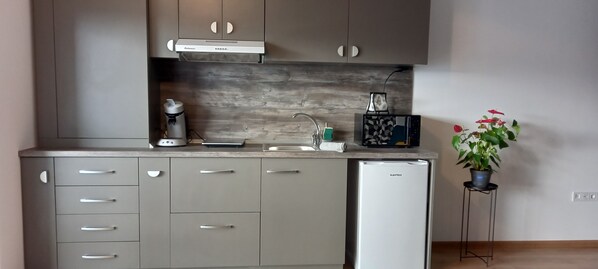 Una cocina con gabinetes grises, horno empotrado, cafetera, tostadora y refrigerador.