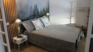 Une chambre à coucher comprenant un lit, deux lampes de chevet, une table de chevet, un panneau mural en bois et une fresque murale représentant une forêt.