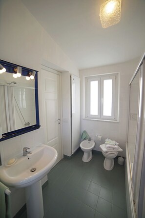A bathroom with a sink, two toilets, a bidet, a mirror, and a window. - Villa Flores a Mondello (Palermo)