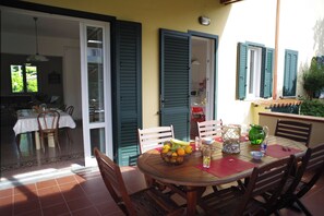 An outdoor dining area with a round wooden table, chairs, and a bowl of fruit. - Villa Flores a Mondello (Palermo)