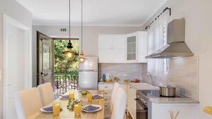 Una cocina moderna con armarios blancos, una campana extractora de acero inoxidable y un comedor con una mesa de madera dispuesta para dos personas.