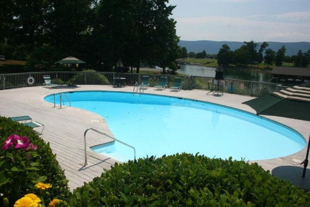 Una piscina con cubierta de madera, rodeada de vegetación y vistas a un lago y montañas.