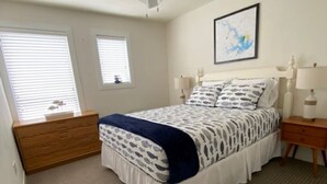 Un dormitorio con una cama, un ventilador de techo, un aparador, dos mesitas de noche con lámparas y un cuadro en la pared.