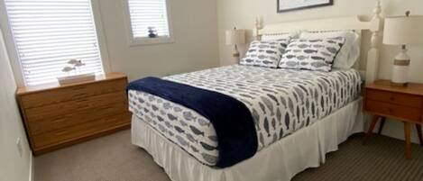 A bedroom with a bed, a ceiling fan, a dresser, two bedside tables with lamps, and a framed picture on the wall.