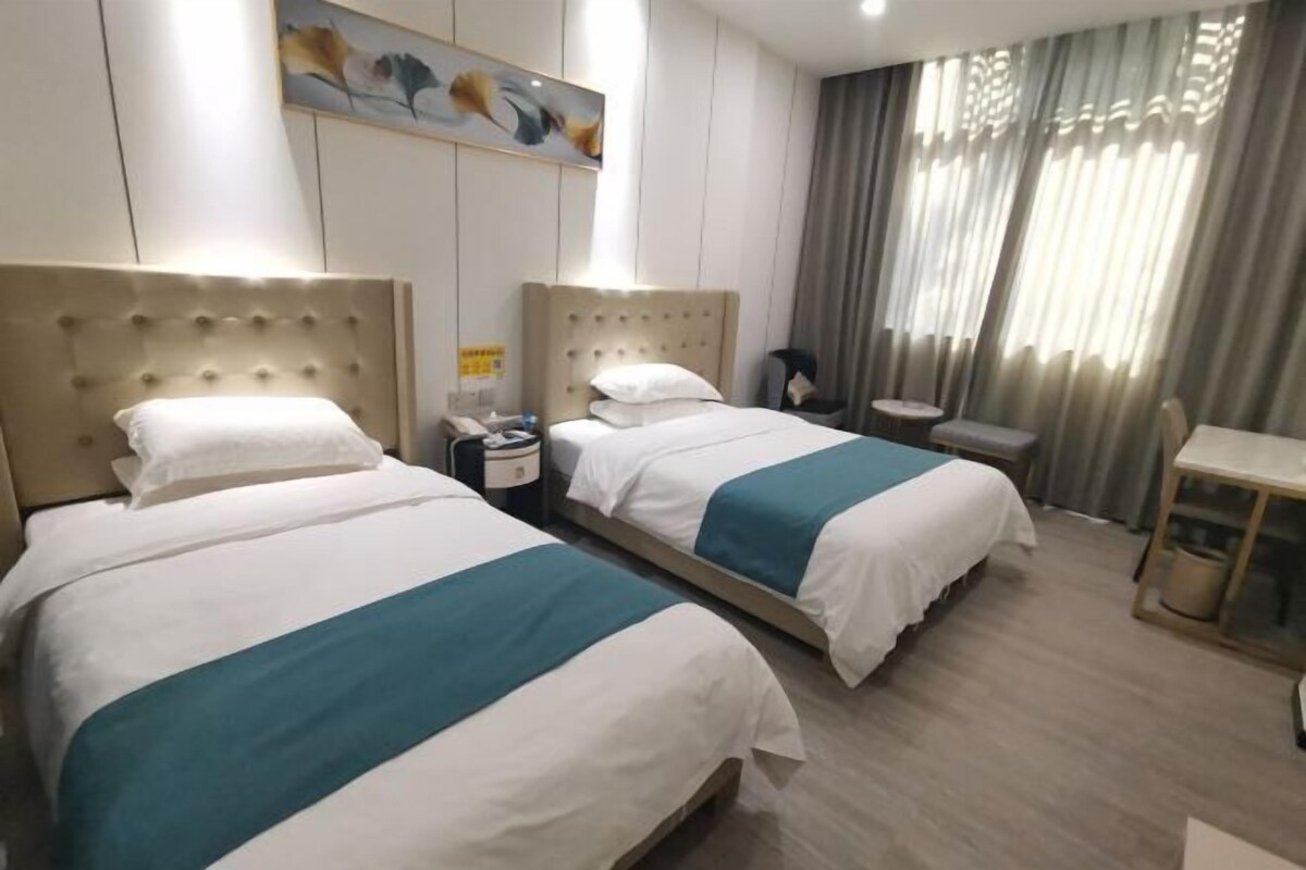A hotel room with two beds, a small table, a chair, a painting on the wall, and a curtain.