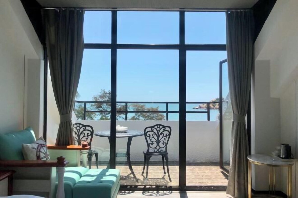 A room with a large window, a sofa, a table, and chairs.
