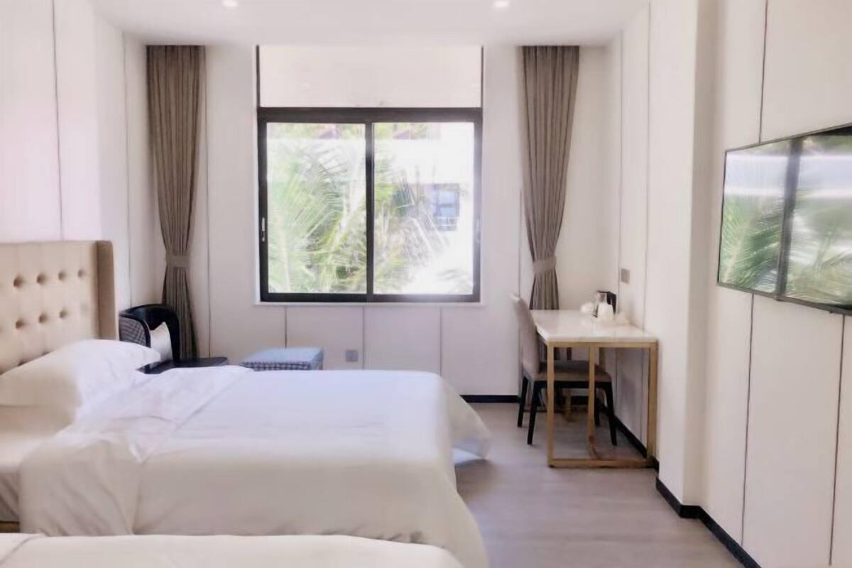 Habitación de hotel con dos camas, un escritorio y un ventanal grande con cortinas.