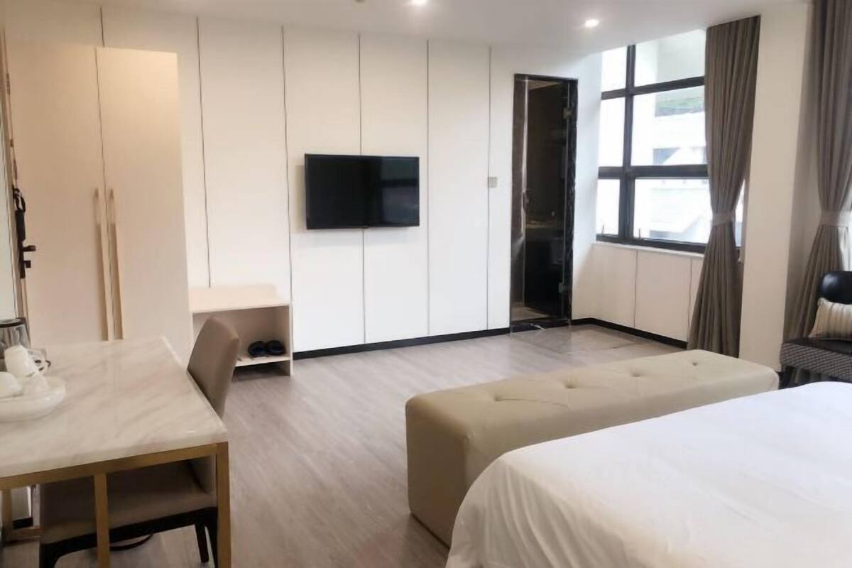 Una habitación de hotel moderna con cama, televisor, zona de estar y ventana con cortinas.