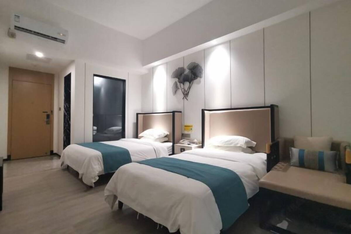Habitación de hotel con dos camas, una mesita de noche y un aire acondicionado de pared.