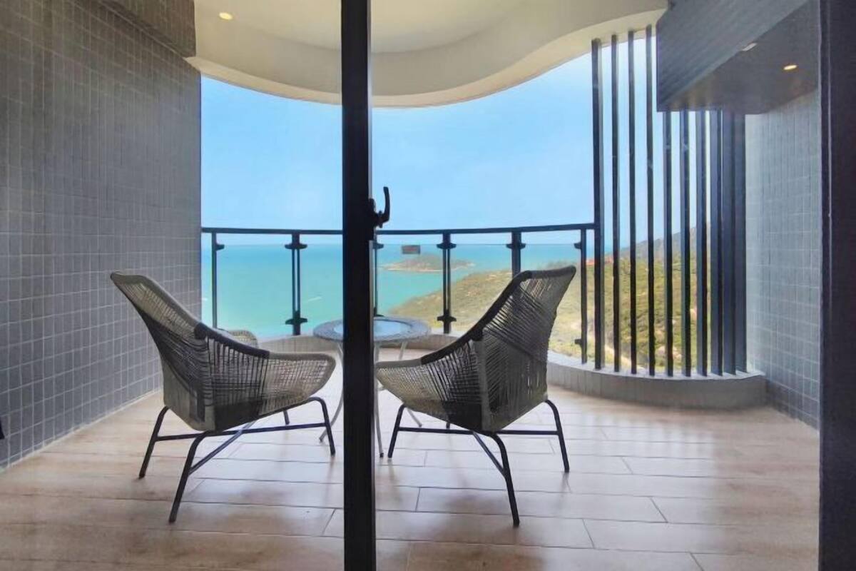 Un balcón con dos sillas de mimbre, una mesa de vidrio y vista al mar.