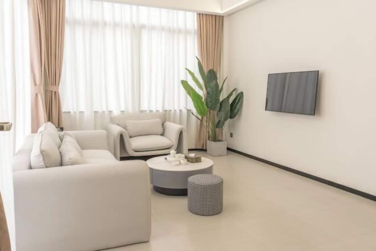 Una sala de estar moderna con un sofá, una mesa redonda de centro, una planta en maceta y un televisor de pantalla plana montado en la pared.