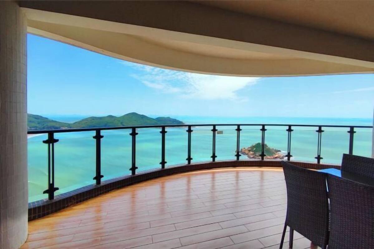 Un balcón con vistas al mar y a las montañas, amueblado con sillas y una mesa.