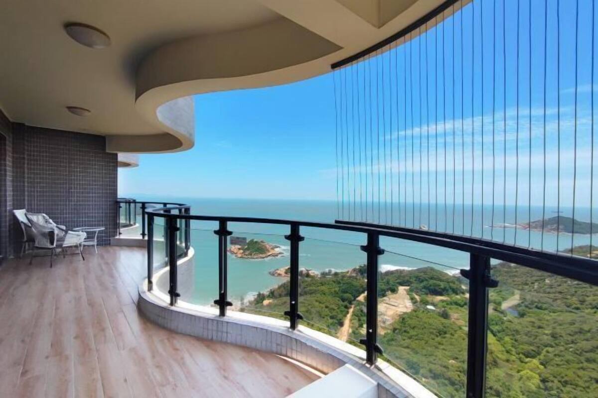 Un balcón con barandilla curva, vista al mar y una pequeña isla.
