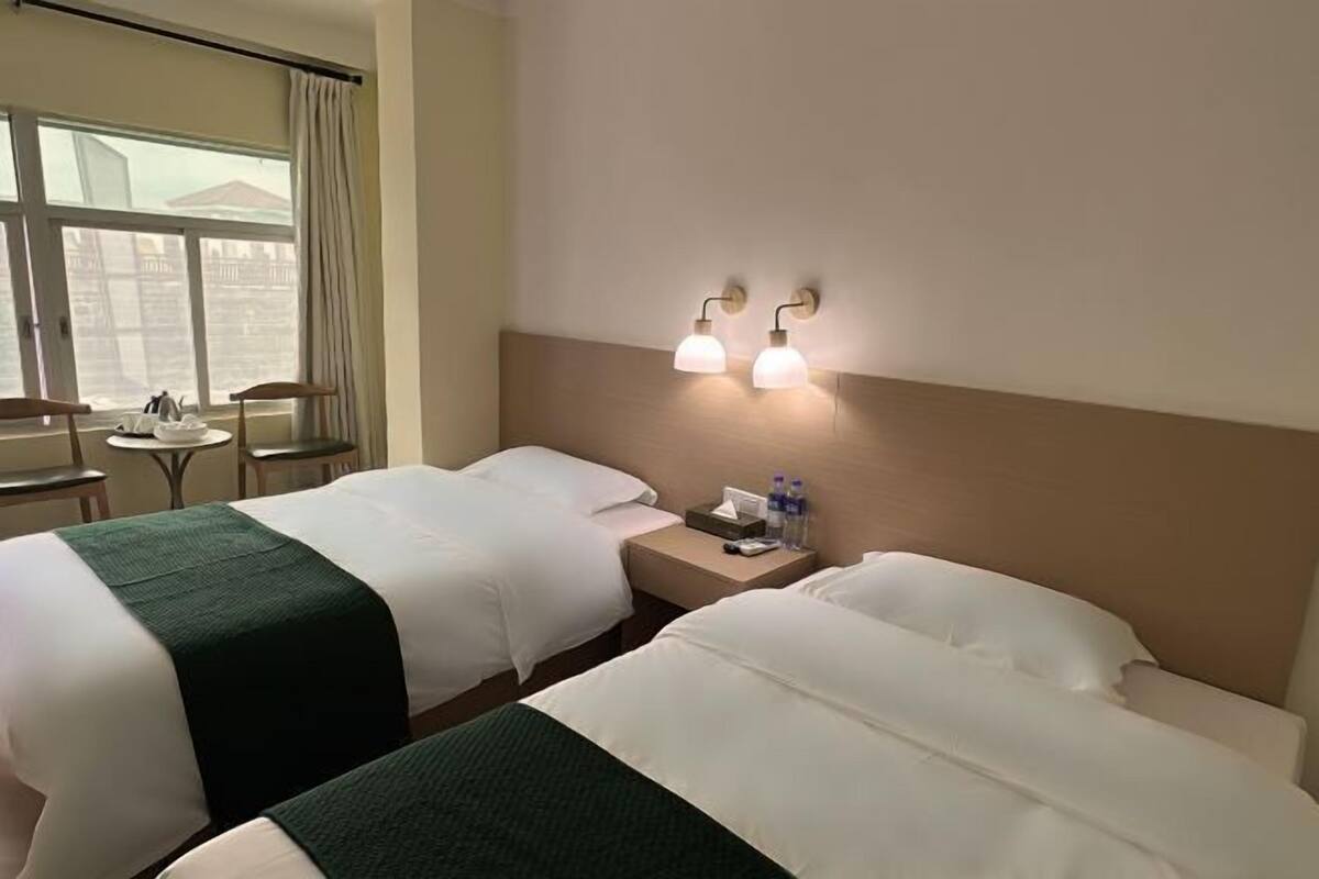 Habitación de hotel con dos camas, una mesita, una silla y una ventana con cortinas.