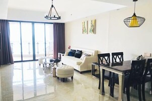 Una sala de estar moderna con sofá, mesa de comedor y sillas. Hay un ventanal con cortinas y una obra de arte en la pared.