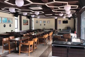 A restaurant with multiple tables and chairs, a counter, and a seating area with couches. - Peninsula Holiday Hotel (Nan'ao County)