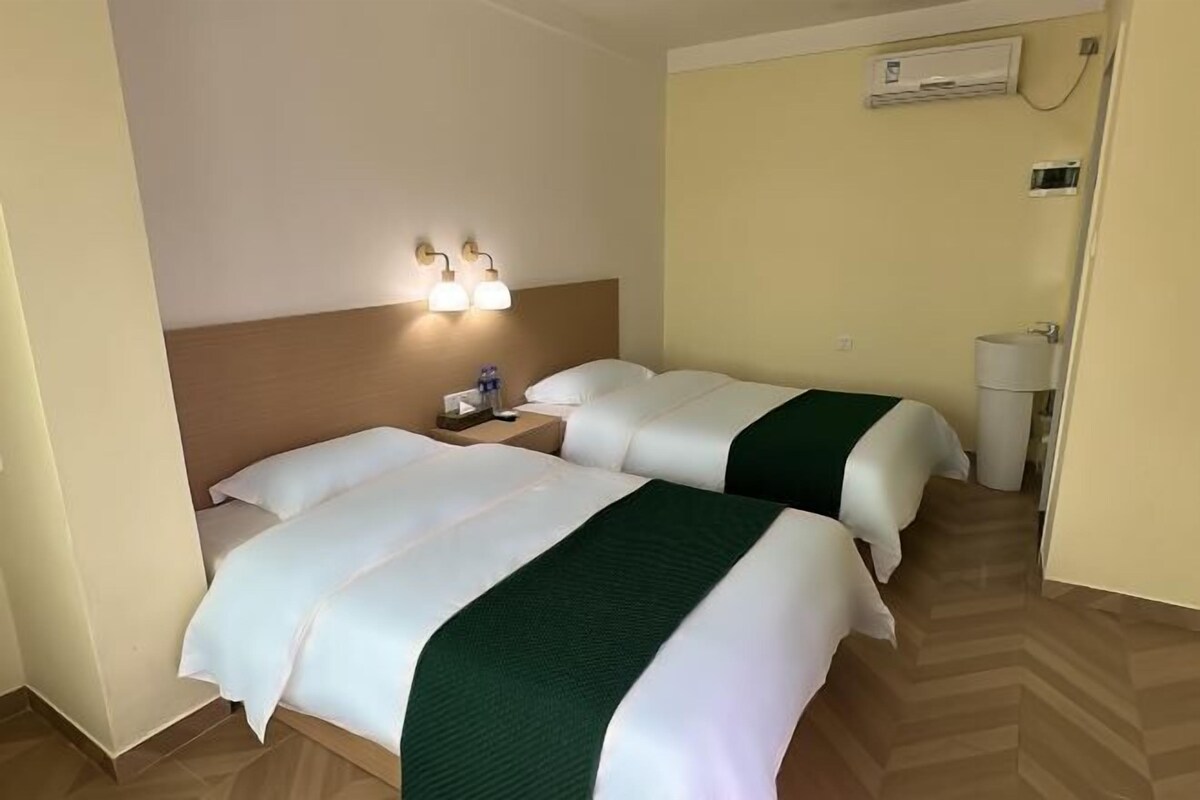 A hotel room with two beds, a nightstand, a lamp, and an air conditioning unit.